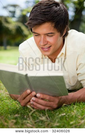 Sorrisi uomo mentre legge un libro come lui giace prono sull'erba