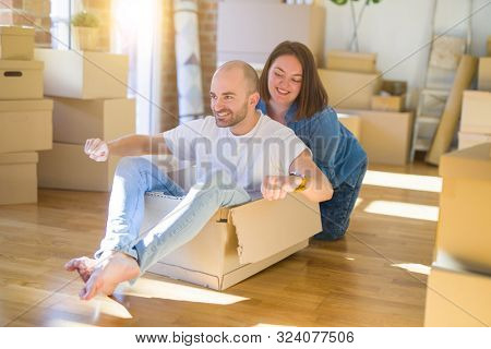 Funny and crazy couple having fun riding a cardboad box as a car, smiling happy and lauging at new home