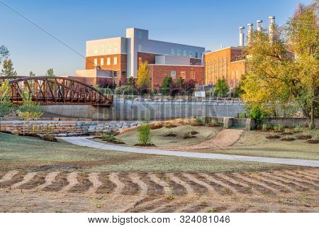landscaping and restoration of natural grass and vegetation in a newly constructed whitewater park on the Poudre River in downtown of Fort Collins Colorado with Powerhouse Energy Campus in background