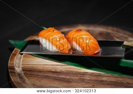 Sushi Salmon Nigiri With Decoration On Top, Served On Japanese Knife On Round Wooden Board With Dark