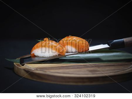 Sushi Salmon Nigiri With Decoration On Top, Served On Japanese Knife On Round Wooden Board With Dark