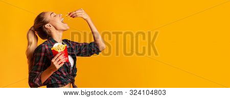 Cheerful Girl Eating French-fried Potatoes Over Yellow Studio Background. Cheat Meal And Fast Food. 