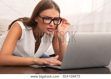 Eyesight. Young Woman Looking Through Eyeglasses At Laptop Having Near Vision Problem Sitting On Cou