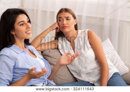 Envy. Jealous Girl Listening To Her Friend Talking About Her Great Life Sitting On Couch At Home. Se