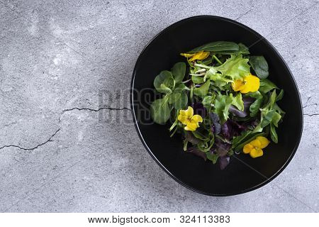 Tasty Healthy Vegan Salad Bowl With Greens, Vegetables And Flowers On Grey Stone Background. Healthy