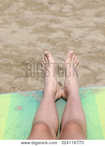 Two Feet Of A Little Girl On The Deck Chair On The Sandy Beach In Summer