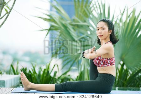 Portrait Of Asian Young Flaxible Woman Sitting On Exercise Mat And Looking At Camera While Exercisin