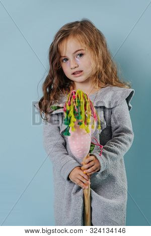 Portrait Of A Little Girl Riding On A Hobbyhorse Over Blue Background