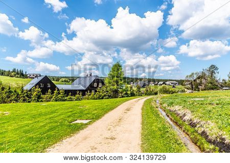 Sunny Summer Day In Jizerka Mountain Village. Dusty Country Road, Green Meadows And Blue Sky With Wh