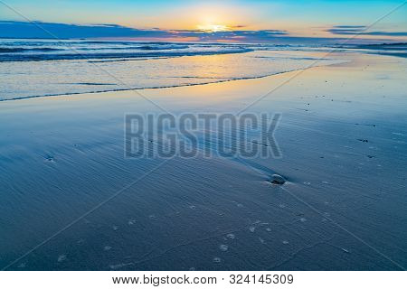Oceanbeach As Sun Is On Horizon Creating Golden Glow Across Sea To Beach Still In Dark Of Morning.