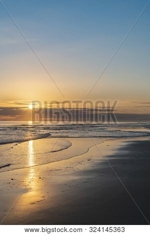 Oceanbeach As Sun Is On Horizon Creating Golden Glow Across Sea To Beach Still In Dark Of Morning.
