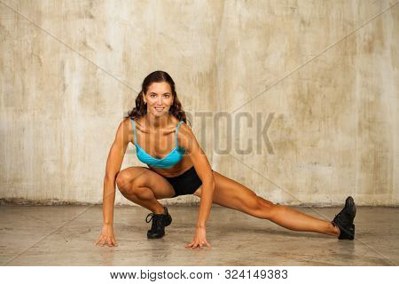 Fintess female body. Full-length portrait of a young athletic girl in black shorts posing against a studio beige wall