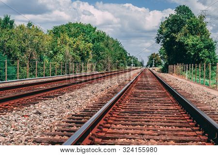 View of train tracks in Houston, TX going into the distance with tress lining the tracks and fence to both sides.