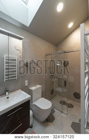 Bathroom In The Attic. On The Wall -  Towel Radiator. Shower Behind Transparent Partition. White Toi