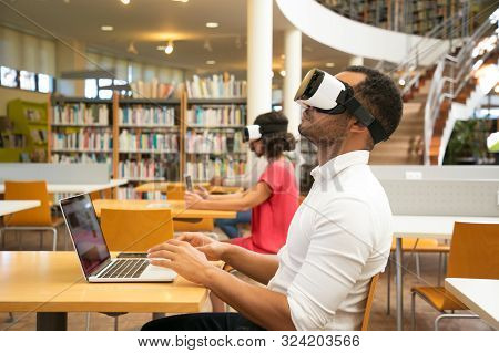 Adult Male Student Training With Vr Simulator In Library. Man Wearing Virtual Reality Glasses, Sitti