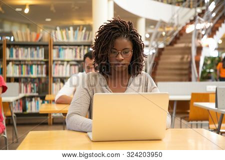 Serious African American Student Working On Research In Library. Students Sitting At Desks And Using