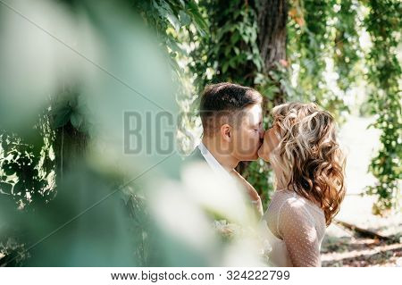 Portrait Of Kissing Couple In The Garden. View Through Tree Foliage