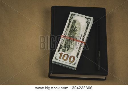 A Black Notebook , A Pen And Dollar Cash Banknotes On Wooden Background - Concept Of Financial Manag