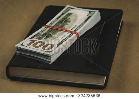 A Black Notebook , A Pen And Dollar Cash Banknotes On Wooden Background - Concept Of Financial Manag