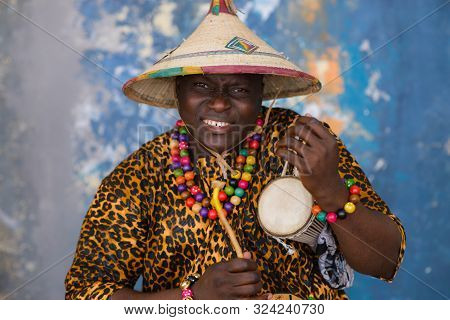 African Man In Traditional Clothes And Fulani Hat Playing On Talking Drum