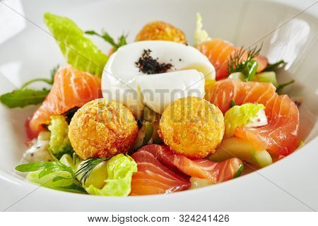Beautiful Restaurant Plate of Trout Fillet 48 Degrees and Egg Poached with Warm Potatoes. Exquisite Italian Arancino and Smoked Salmon or Sliced Red Fish on Natural Black Marble Background