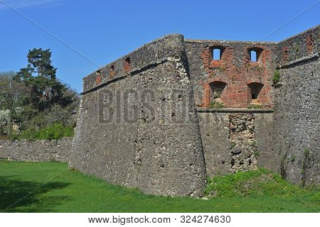 Uzhgorod Fortress Against Blue Sky Background. Old Moat Overgrown With Grass In Foreground.