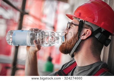 Construction Mason Worker Sitting High On The Scaffolding, Resting And Drinking Water