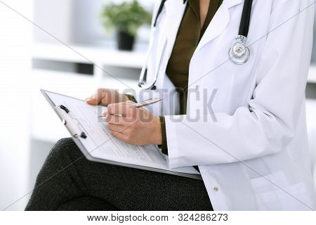 Woman Doctor Writing Something At Clipboard While Sitting At The Chair, Close-up. Therapist At Work 