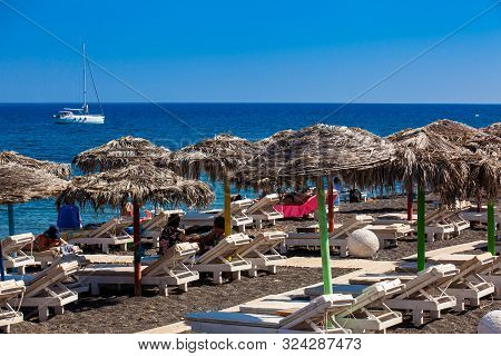Santorini, Greece - April, 2018: Tourists Sunbathing At The Beautiful Perissa Village Beach In Santo