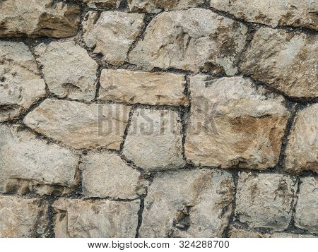 Stone Ancient Wall Paved With Cobble Stones, Closeup. Old Brown And Gray Cobblestone Wall Texture. N