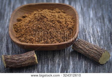 Liquorice Stick And Ground Herbs In Wooden Bowl On Textured Surface