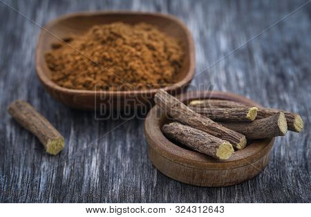 Liquorice Stick And Ground Herbs In Wooden Bowl On Textured Surface