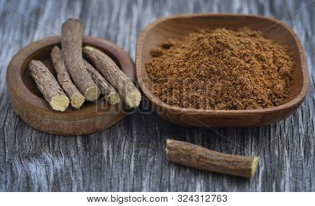 Liquorice Stick And Ground Herbs In Wooden Bowl On Textured Surface