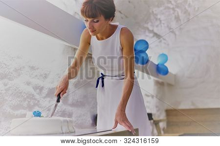 Young Woman In A White Dress Cuts A Wedding Cake With A Knife