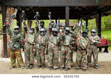 Drenge klædt i camouflage stå i træk på en paintball base, oprejser sin paintball pistol.