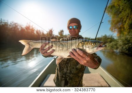 Happy angler holds Asp fish (Aspius aspius) being on the boat and smiles. Astrakhan region, Russia
