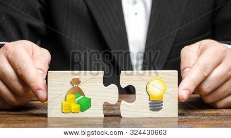 Businessman Puts Two Puzzles With The Image Of Money And An Idea Bulb. Financing Promising Startups 