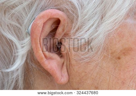 Hearing Aid. Female Pensioner With White Hair Wearing A Behind The Ear, Bte, Hearing Aid. Close Up O