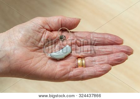Hearing Aid. Female Pensioner Holding A Behind The Ear, Bte, Hearing Aid In The Palm Of Her Hand.