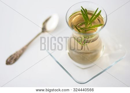 Rosemary Tea In Armudu Glass With Branch Of Rosemary In It And Spoon On The Table On White Backgroun