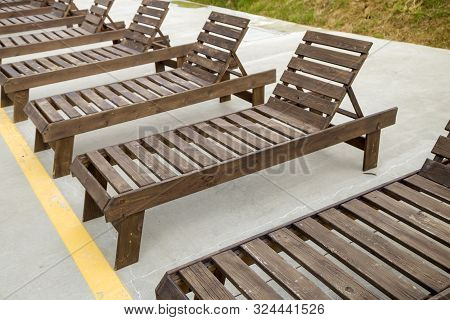 Row Of Empty Wooden Beach Chairs Near Water Outdoors.