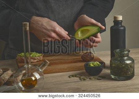 Chef Making Avocado Sandwiches With Bread, Nuts, Herbs  And Avocado Oil On A Wooden Table. Man Makin