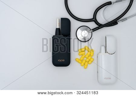Iqos, Stethoscope And Yellow Pills On A White Background. The Concept Of Health Damage From Smoking 