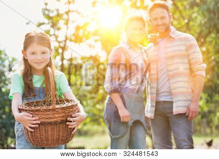 Mother and father with daughter are collecting eggs and putting them in a brown wicker baset, concept organic family lifestyle