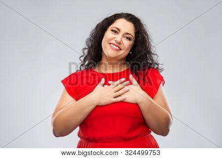 appreciation, love and sincere emotions concept - happy woman in red dress holding hands on chest or heart over grey background