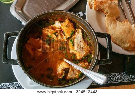 Kharcho Soup With Meat And Rice In A Cast-iron Bowl On A Wooden Table, Georgian Bread Is Next To It.