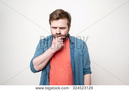 Pensive Man Touches His Bearded Chin With His Hand And Looks Sternly At The Camera. Isolated On Whit