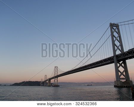 San Francisco Side Of Bay Bridge At Dusk With Oakland In The Distance On A Clear Day.
