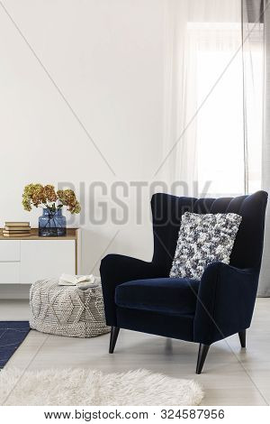 Books And Flowers On Console Table In White Living Room Interior With Velvet Wing Back Chair With Pa