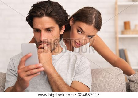 Distrust. Jealous Wife Spying On Cheating Husband While He Texting On Phone Standing Behind His Back